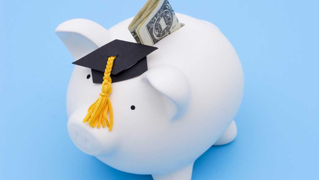 White piggy bank wearing a graduation cap with cash sticking out, symbolizing tuition costs and student savings.